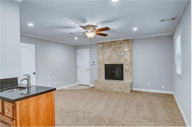 unfurnished living room featuring light colored carpet, ceiling fan, crown molding, sink, and a fireplace