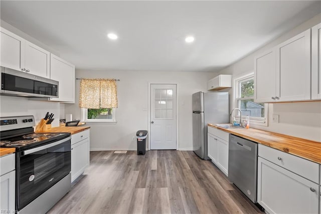 kitchen with stainless steel appliances, white cabinetry, and butcher block countertops