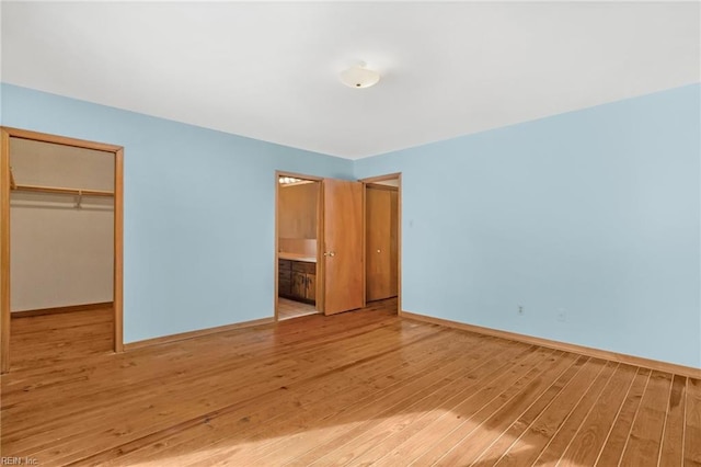 unfurnished bedroom featuring ensuite bath, a closet, a walk in closet, and light wood-type flooring