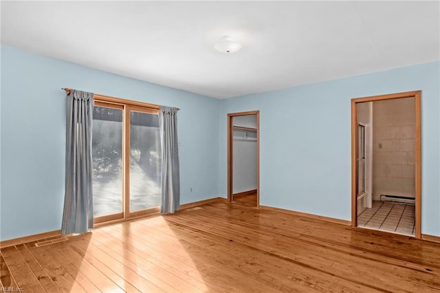 unfurnished bedroom featuring a baseboard radiator, connected bathroom, light hardwood / wood-style flooring, and a closet