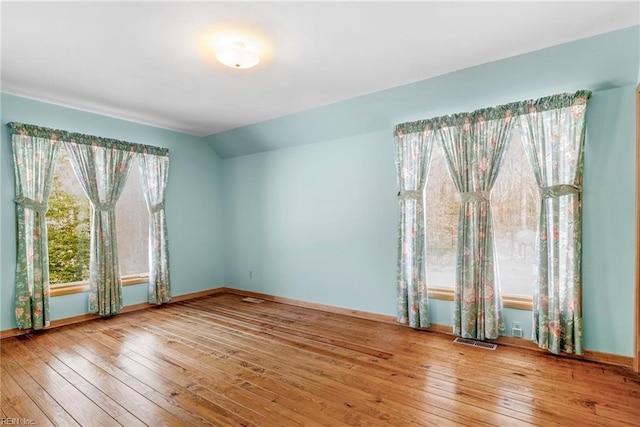 empty room with a wealth of natural light, lofted ceiling, and hardwood / wood-style floors