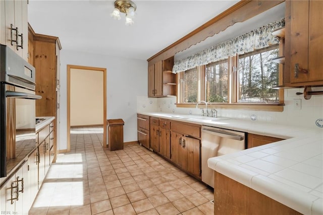 kitchen featuring dishwasher, sink, tile counters, light tile patterned floors, and black oven