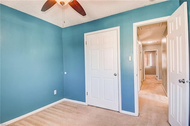 unfurnished bedroom featuring light carpet, a textured ceiling, a closet, and ceiling fan