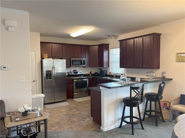 kitchen with kitchen peninsula, a textured ceiling, stainless steel appliances, sink, and a breakfast bar area