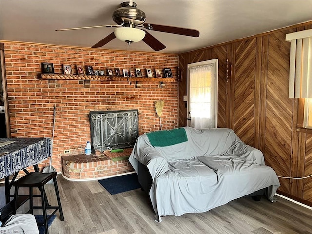 living room with wood-type flooring, ceiling fan, wood walls, and brick wall
