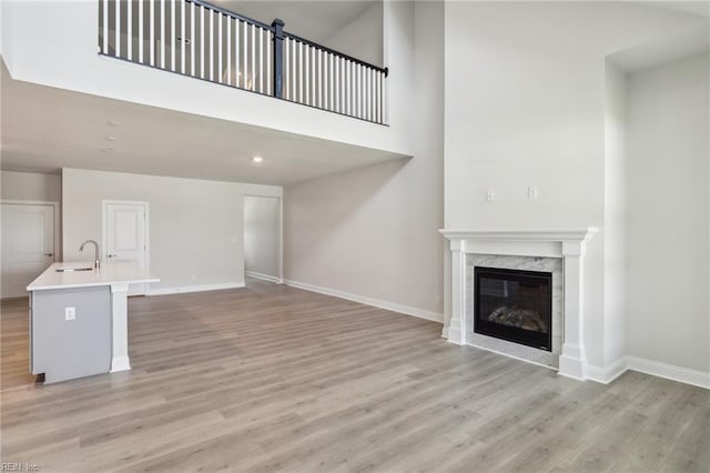 unfurnished living room with light hardwood / wood-style floors, a premium fireplace, sink, and a high ceiling