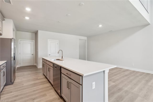 kitchen featuring appliances with stainless steel finishes, a center island with sink, light hardwood / wood-style flooring, and sink