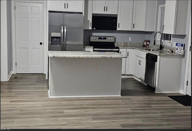 kitchen with light stone countertops, stainless steel appliances, sink, white cabinets, and a center island