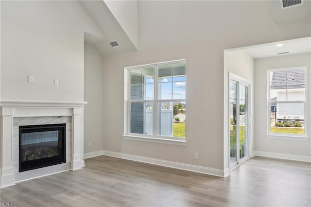 unfurnished living room with a high end fireplace, lofted ceiling, and light wood-type flooring