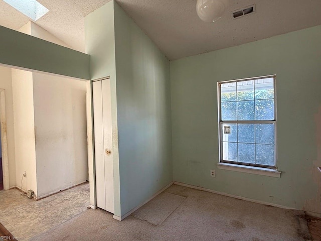 spare room with vaulted ceiling with skylight and a textured ceiling