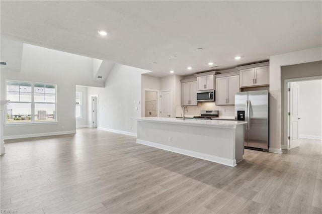 kitchen featuring gray cabinetry, stainless steel appliances, light hardwood / wood-style floors, decorative backsplash, and a center island with sink