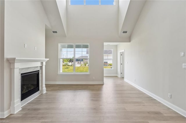 unfurnished living room with a fireplace, a towering ceiling, and light wood-type flooring