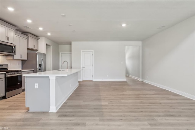 kitchen with sink, gray cabinets, an island with sink, appliances with stainless steel finishes, and light hardwood / wood-style floors