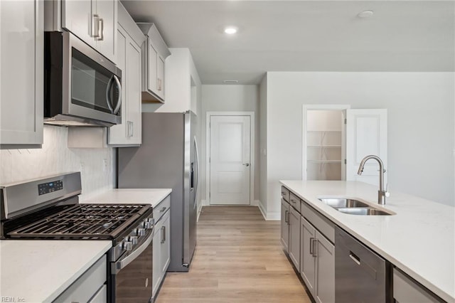 kitchen with tasteful backsplash, gray cabinetry, stainless steel appliances, sink, and light hardwood / wood-style floors