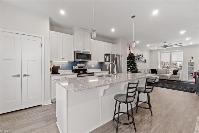 kitchen featuring hanging light fixtures, ceiling fan, an island with sink, appliances with stainless steel finishes, and white cabinetry