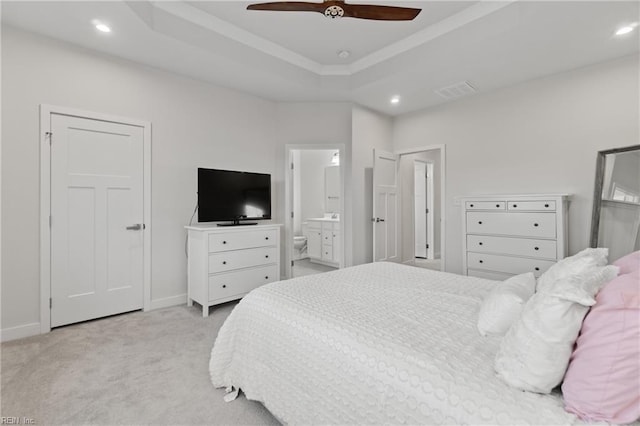 bedroom featuring a tray ceiling, ensuite bath, ceiling fan, and light carpet