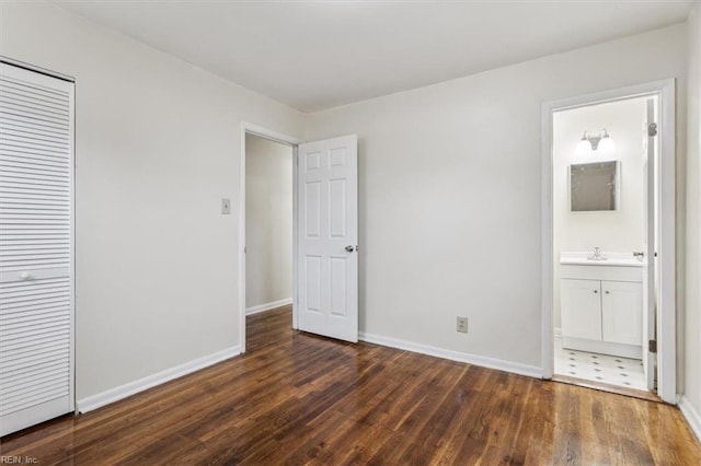 unfurnished bedroom featuring ensuite bath, a closet, dark wood-type flooring, and sink