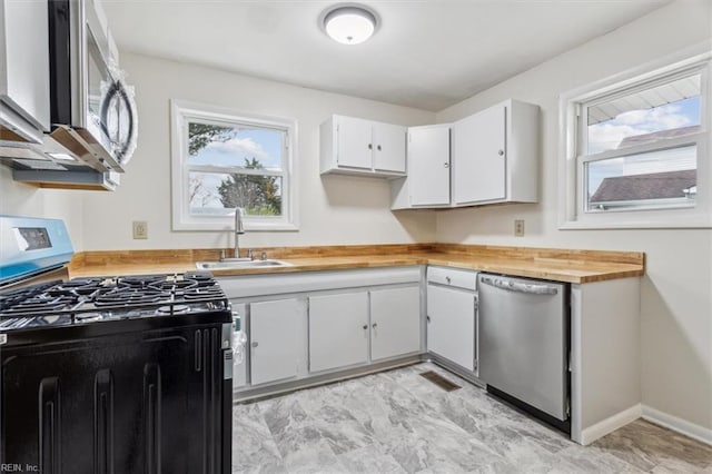 kitchen with wood counters, stainless steel appliances, white cabinetry, and sink