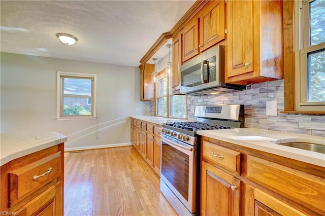 kitchen with hanging light fixtures, stainless steel appliances, light stone counters, light hardwood / wood-style floors, and decorative backsplash