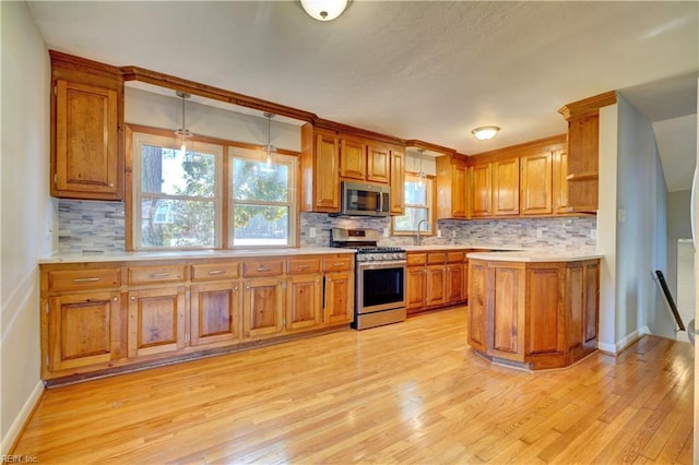 kitchen featuring backsplash, decorative light fixtures, stainless steel appliances, and light hardwood / wood-style flooring