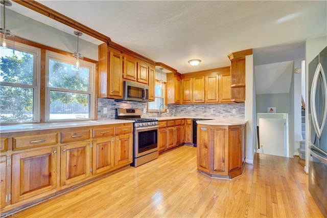 kitchen featuring light wood-type flooring, stainless steel appliances, hanging light fixtures, and tasteful backsplash