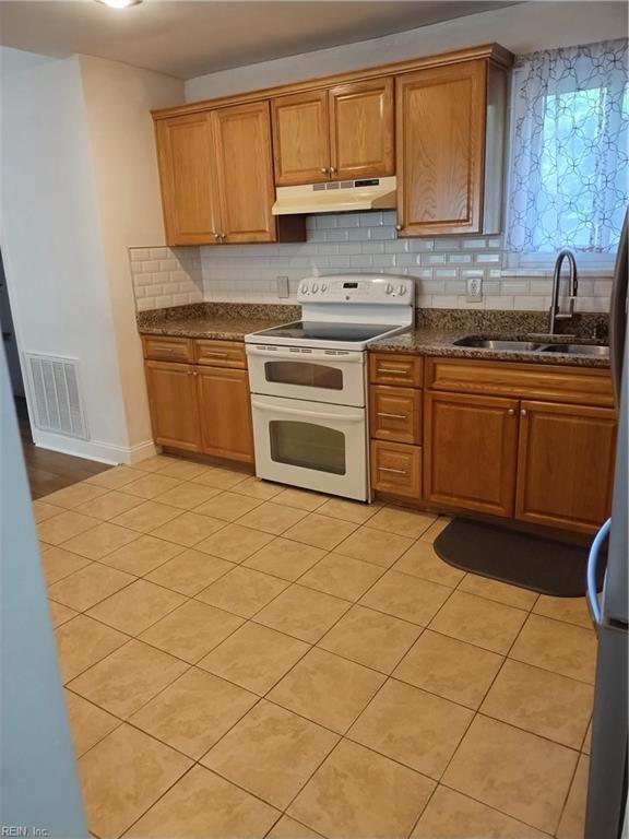 kitchen with sink, white range with electric cooktop, dark stone countertops, decorative backsplash, and light tile patterned floors