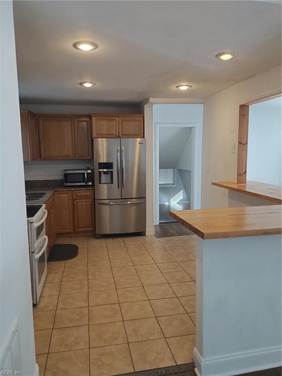 kitchen with decorative backsplash, light tile patterned floors, appliances with stainless steel finishes, butcher block countertops, and kitchen peninsula