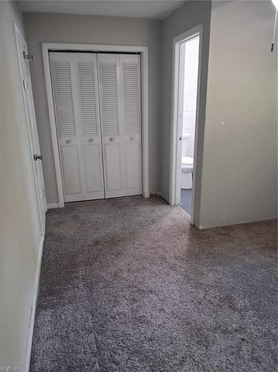 unfurnished bedroom featuring ensuite bath, dark carpet, and a closet