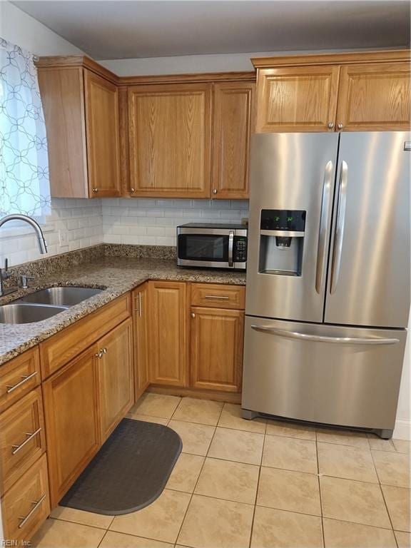 kitchen featuring backsplash, dark stone counters, sink, light tile patterned flooring, and stainless steel appliances