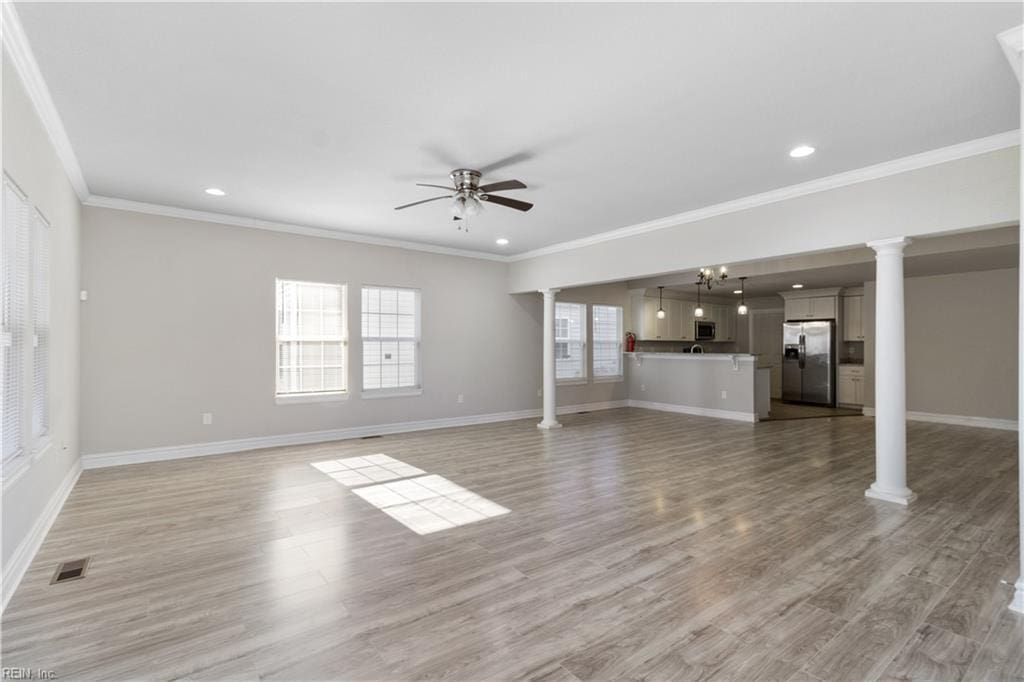 unfurnished living room featuring ceiling fan with notable chandelier, crown molding, and light hardwood / wood-style flooring