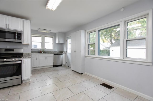 kitchen featuring white cabinets, light tile patterned flooring, light stone counters, and appliances with stainless steel finishes