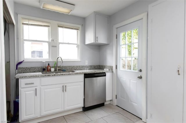 kitchen featuring dishwasher, sink, light tile patterned floors, light stone counters, and white cabinetry