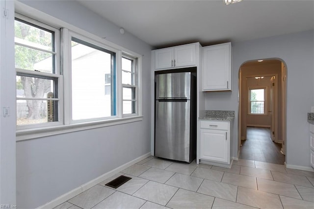 kitchen with stainless steel refrigerator, white cabinets, a healthy amount of sunlight, and light tile patterned floors