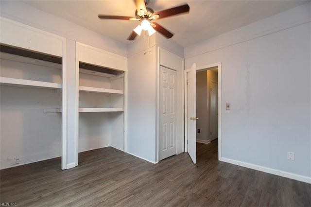 unfurnished bedroom with ceiling fan, dark hardwood / wood-style floors, and two closets