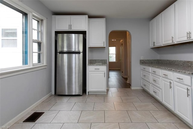 kitchen featuring white cabinets, light tile patterned flooring, stainless steel refrigerator, and light stone counters