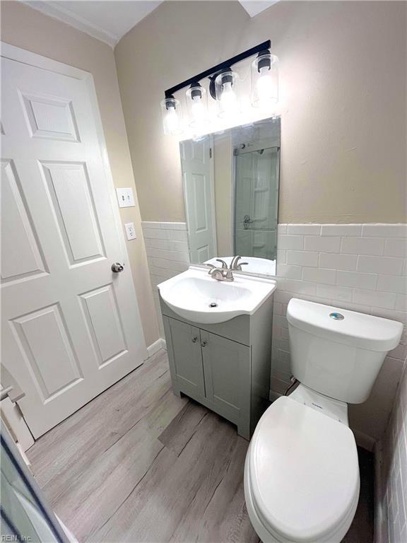 bathroom with wood-type flooring, vanity, toilet, and tile walls