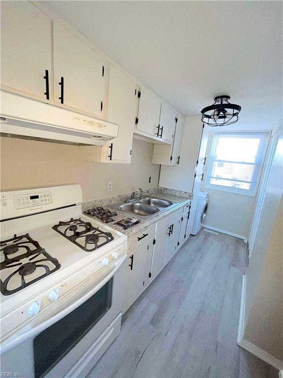 kitchen with white cabinets, sink, light wood-type flooring, white range with gas stovetop, and a chandelier