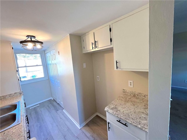 kitchen featuring white cabinetry, light stone countertops, sink, and light wood-type flooring