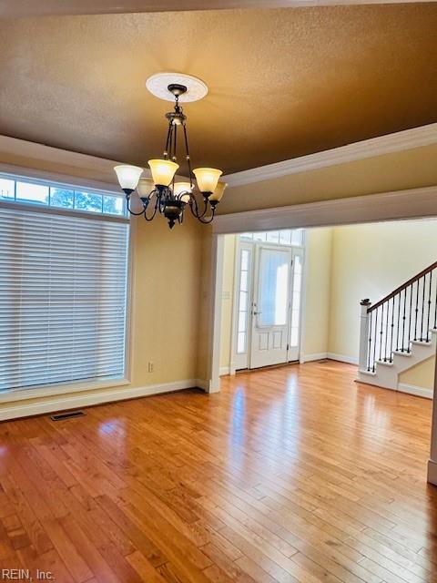 unfurnished room with a chandelier, a textured ceiling, light hardwood / wood-style flooring, and ornamental molding