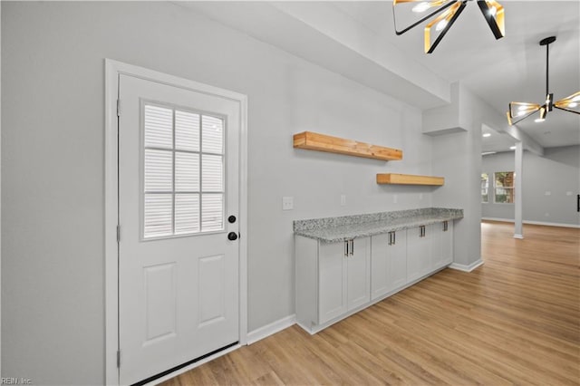 kitchen with pendant lighting, light wood-type flooring, white cabinetry, and an inviting chandelier