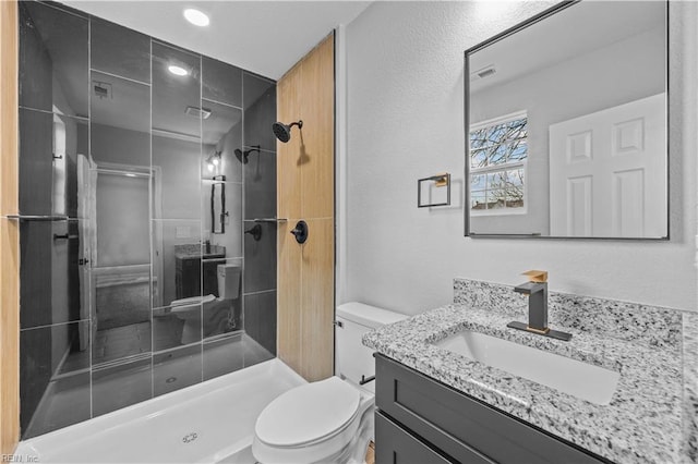 bathroom with a tile shower, vanity, and toilet