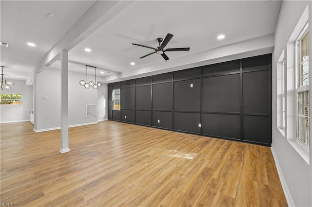 unfurnished living room with ceiling fan with notable chandelier and light hardwood / wood-style flooring