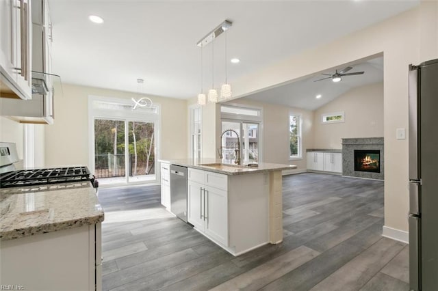 kitchen with light stone counters, stainless steel appliances, a center island with sink, white cabinetry, and hanging light fixtures