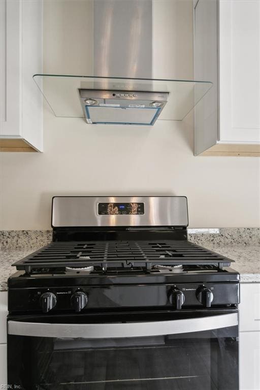 interior details with wall chimney exhaust hood, white cabinetry, and stainless steel range with gas stovetop