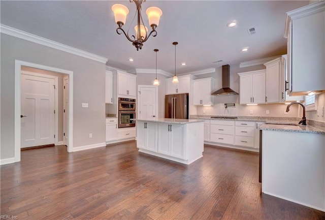 kitchen featuring stainless steel appliances, sink, wall chimney range hood, white cabinetry, and a kitchen island