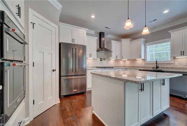 kitchen featuring a center island, wall chimney exhaust hood, light stone counters, white cabinetry, and stainless steel appliances