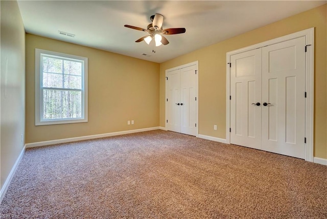 unfurnished bedroom with carpet, ceiling fan, and two closets