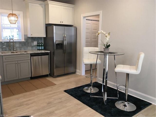 kitchen featuring white cabinets, sink, hanging light fixtures, light wood-type flooring, and stainless steel appliances