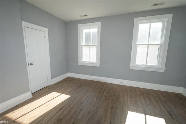 empty room with a wealth of natural light and dark hardwood / wood-style flooring