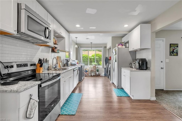 kitchen featuring light stone countertops, appliances with stainless steel finishes, white cabinets, hardwood / wood-style floors, and hanging light fixtures